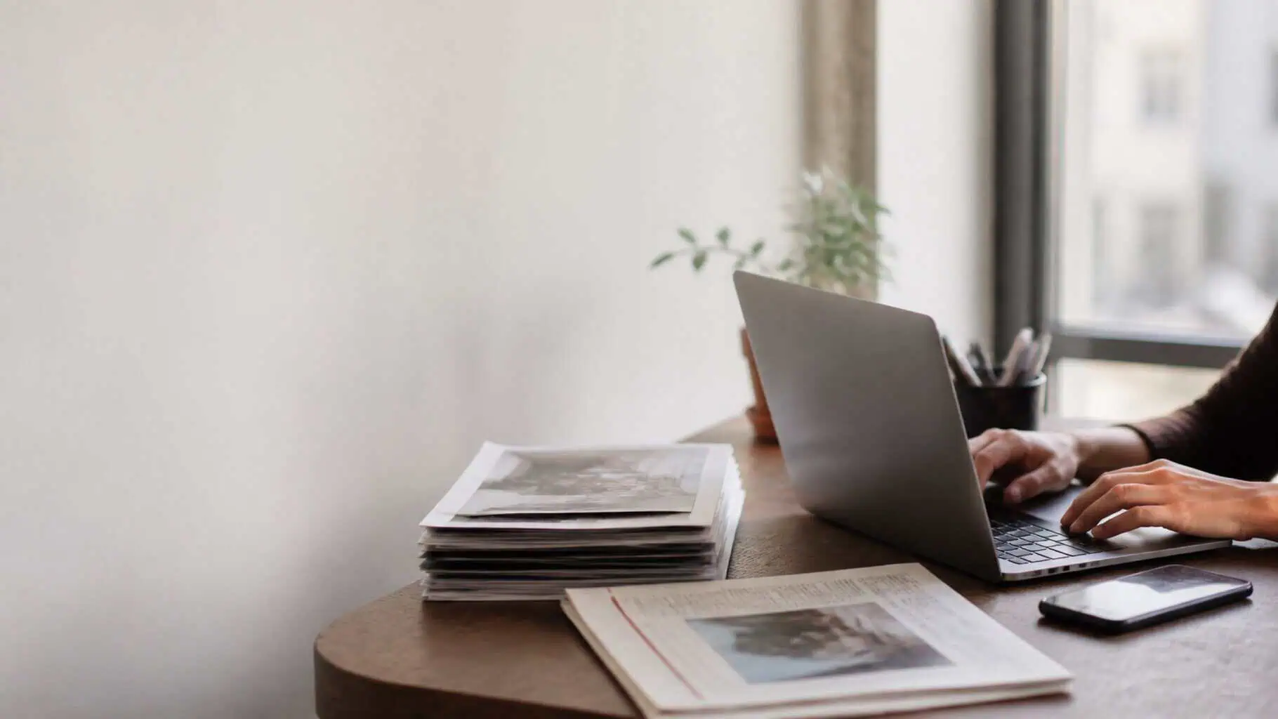 Printed flyers and a newspaper on one side of a desk, a laptop and phone on the other